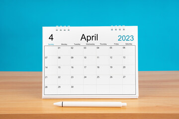 The April monthly desk calendar for 2024 year and pen on wooden table with blue color background.