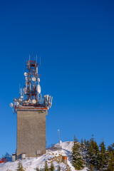 Naklejka premium Tower of telecommunication with many antennas, in a beautiful winter mountains landscape, with trees covered in snow and copy space.