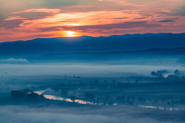 Aerial view of the sunrise over the valley in beautiful early morning mist in the highlands. Low clouds and fog cover the sleeping meadow. Hills valley mists landscape. Serene moment in rural area
