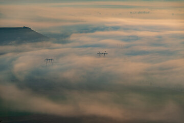 Aerial view of the valley in early morning mist, beautiful in the highlands. Low clouds and fog cover the sleeping meadow. Alpine mountain valley mists landscape at dawn. Serene moment in rural area