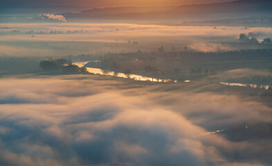Aerial view of the valley in early morning mist, beautiful in the highlands. Low clouds and fog cover the sleeping meadow. Alpine mountain valley mists landscape at dawn. Serene moment in rural area