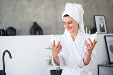 Woman holding dispenser bottles with shampoo in hands at bathroom