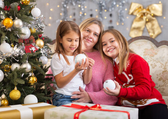 Happy mom with two girls near the Christmas tree in the living room