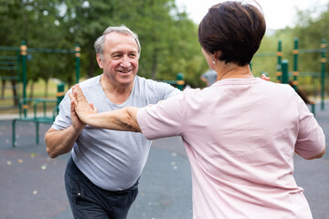 Friendly family couple doing gymnastic exercises together in summer city park