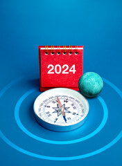 Happy new year 2024 vertical banner background. 3d globe, 2024 numbers year on red desk calendar cover stand and compass on target dartboard and blue background. Worldwide business goals concepts.