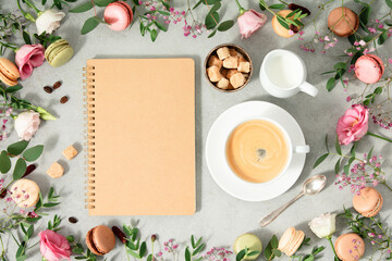 White cup of coffee, empty notebook and Frame made of Spring flowers and different types of macaroons - obrazy, fototapety, plakaty