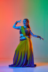 Young beautiful woman in traditional indian dress and makeup dancing against gradient studio background in neon light. Concept of beauty, fashion, India, traditions, lifestyle, choreography, art. Ad