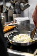 man chef cooking tasty scrambled eggs in frying pan on kitchen