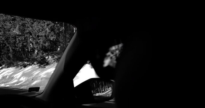 monochrome 4K DCi footage, featuring a close-up of a woman's sunglasses during her drive on a snow-draped rural highway within the mountainous landscape.