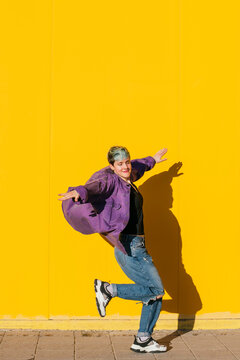 Happy woman with arms outstretched in front of yellow wall