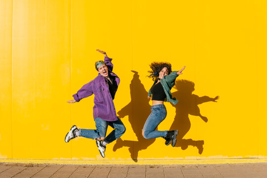 Cheerful lesbian couple jumping in front of yellow wall
