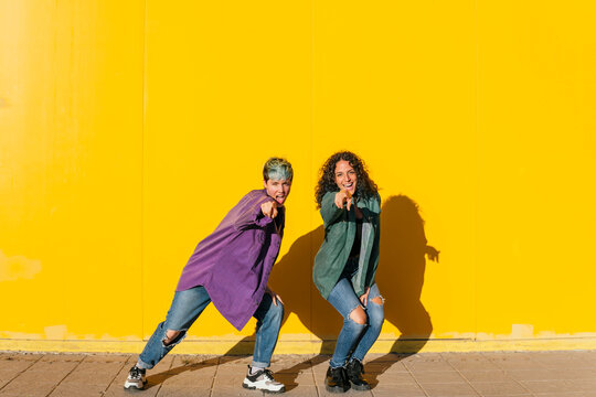 Happy lesbian couple dancing in front of yellow wall