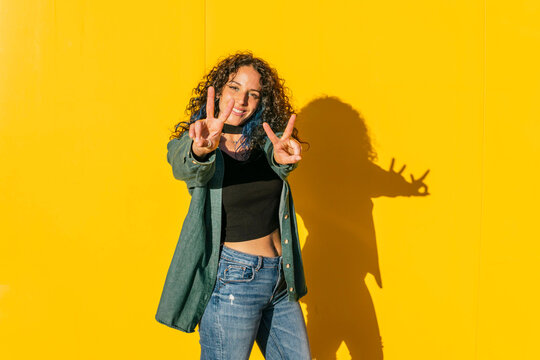 Smiling woman showing peace sign in front of yellow wall