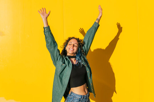 Carefree woman with arms raised in front of yellow wall