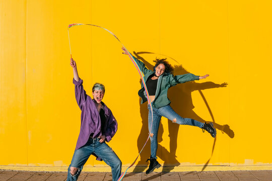 Cheerful lesbian couple having fun in front of yellow wall at sunny day