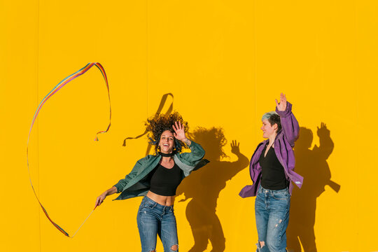Carefree lesbian couple dancing and enjoying in front of yellow wall