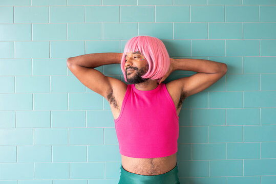 Young Queer Man With Hands Behind Head In Front Of Tiled Wall