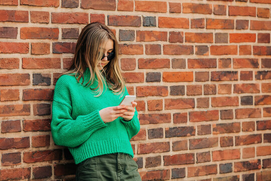 Teenage girl using smart phone leaning on brick wall