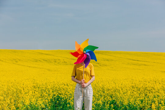 Woman holding colorful pinwheel toy amidst yellow flowers in rapeseed field
