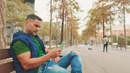 Mature man tourist wearing casual clothes sitting on bench scrolling smartphone