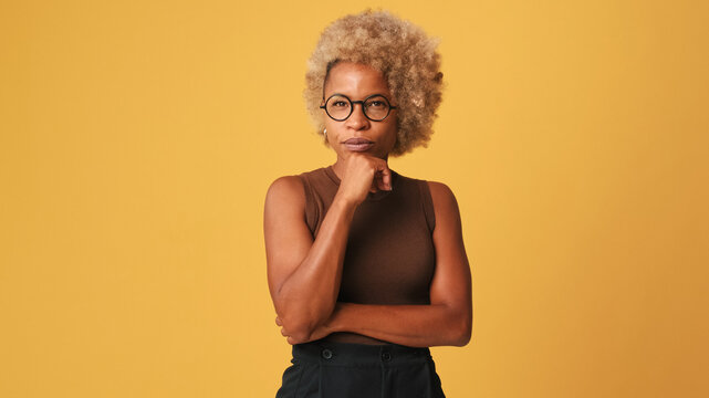 Beautiful girl in glasses, wearing brown top t attentively listens to someone and nods her head in agreement isolated on orange background