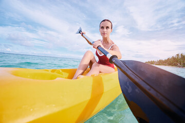 Active vacation. Young woman paddling the sea kayak near tropical bay.