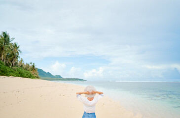 Fototapeta na wymiar Vacation on the seashore. Back view of young woman on the beautiful tropical white sand beach.