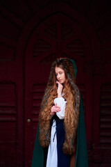 Fairytale princess wearing cloak with medieval castle door on the background.