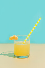 Tangerine juice in a glass with slice and straw. Turquoise and beige background. Minimalism.