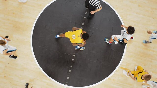 Basketball Tournament Final: Diverse Yellow and White Teams Compete at Center Court for Jump Ball that Starts the Game. Athletic Sportsmen Reach for the Ball. Top Down Cinematic Slow Motion Footage