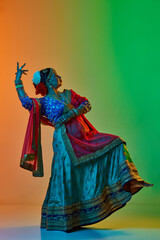 Indian culture. Mature, beautiful indian woman in traditional clothes, dress posing over gradient studio background in neon light. Concept of beauty, fashion, India, traditions, choreography, art. Ad