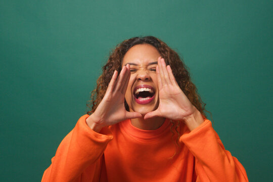 Young biracial woman raises hands, yells excitedly, green background studio