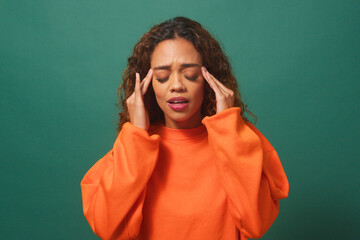 Young multi-ethnic woman rubs temples, headache, green studio background