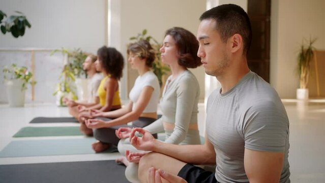 Multiracial friends meditating in row at airy yoga studio