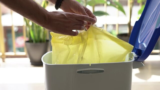 A man takes out a yellow bag of waste from a trash can.