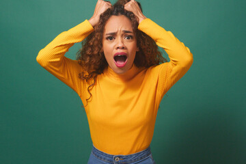 Frustrated and angry young woman 'tears hair out' - green studio background