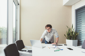 Young contemporary creative businessman indoors office using computer