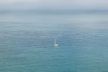 the white boat with the white sail floats on the blue sea.