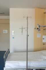 Empty hospital bed with intravenous drip in hospital ward. Medical equipment with a religious symbol hanging on the wall. An empty hospital room with a drip.