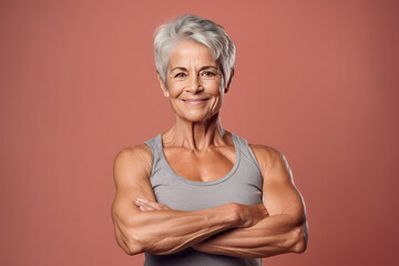 Portrait of elderly smiling woman with a highly muscular physique, old woman bodybuilder isolated on flat color background with copy space.
