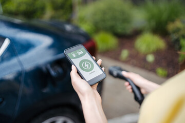 Close up of woman using electric vehicle charging app, checking charging of his electric car.