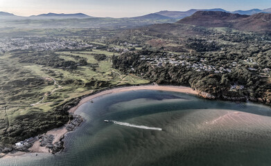 Beautiful sandy bay and blue sea with boats turning in the eater and a mountain in view in Wales, UK