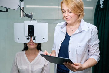 Adult female taking digital refraction test supervised by eye doctor
