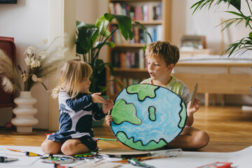 Siblings painting at home with watercolors and tempera paints, creating a model of planet Earth.