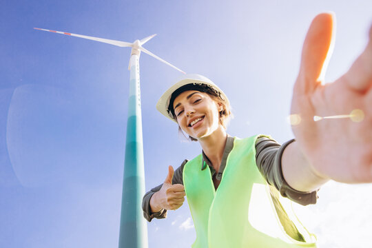 Woman engineer with helmet standing by the windmill turbines