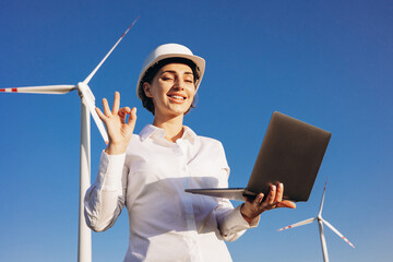 Woman having conference online on laptop at the field with windmill turbines