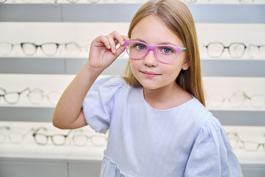 Tranquil little girl trying on eyeglasses in optical shop