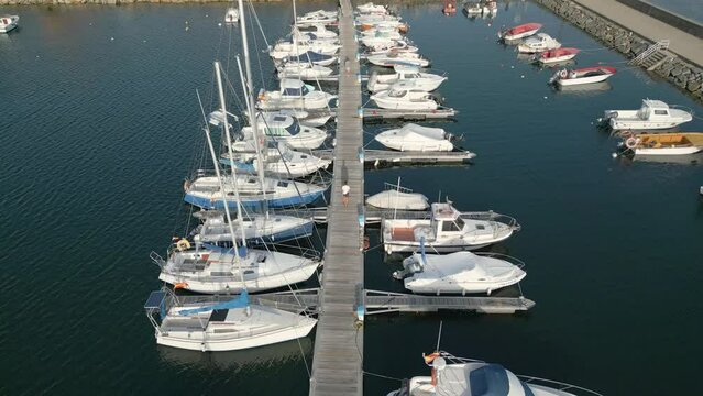 Two People Walking Towards The Port Of Yacht Club At Rianxo In A Coruna, Spain. aerial, tracking shot