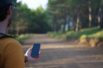 Man consulting smartphone in the forest to avoid getting lost. Travel and adventure concept