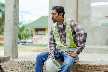 Man wearing green reflective vest Taking off helmet to cool off After working on construction site. Indian foreman had mustache. Taking a break from work and the hot weather until to stop working.